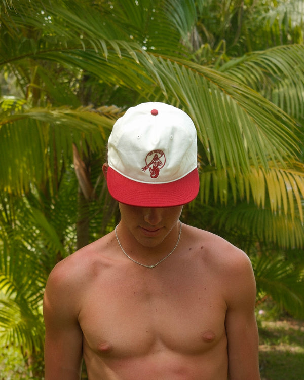 Man wearing a white and red cap with The Merman logo against a tropical background