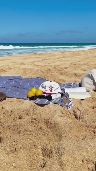 Baseball cap hat snap back with 'The Merman' logo embroidered in red on a cream off white canvas on the beach
